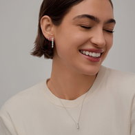 Model wearing a diamond pendant necklace and diamond hoop earrings with a light-colored top.