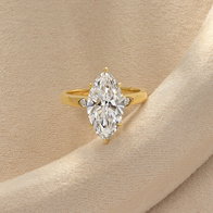 Gold ring featuring a marquise-cut diamond with diamond side accents on a neutral fabric background.