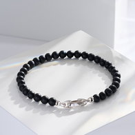 Black beaded bracelet with a polished silver-tone clasp, displayed on a glossy white surface.