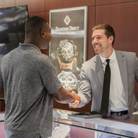 Customer and sales associate shaking hands at a Diamonds Direct showroom counter.