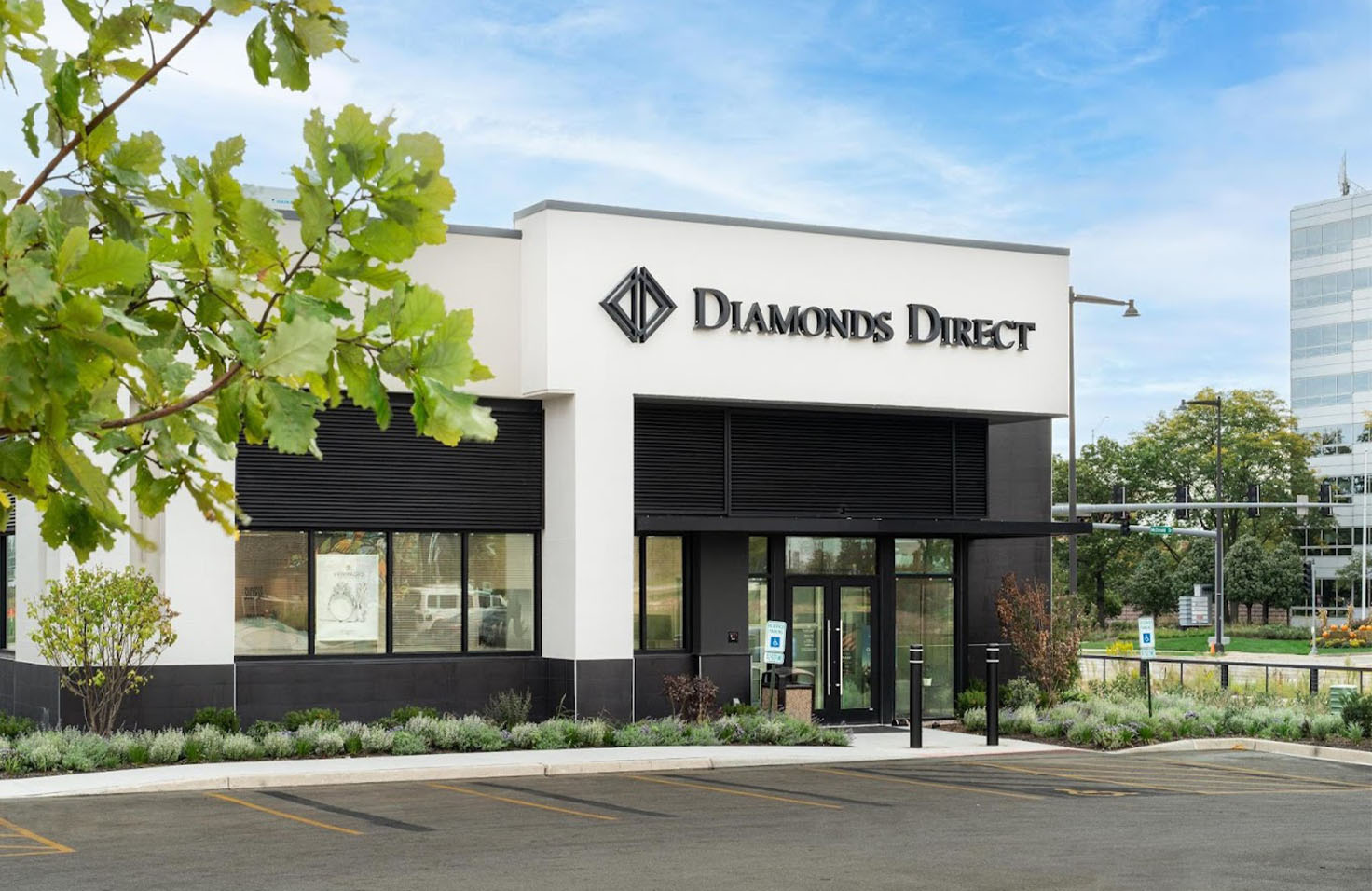 Diamonds Direct jewelry store exterior with modern white facade, black accents, and landscaped entrance.
