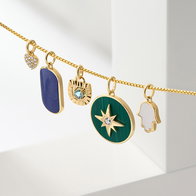 Gold charm necklace featuring stone accent pendants displayed on a white surface.