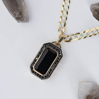 Gold chain necklace with rectangular black gemstone pendant and black accent stones arranged on a white surface.