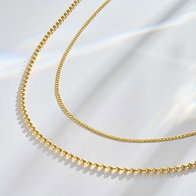 Yellow gold curb chain and beaded ball chain necklaces layered on white fabric