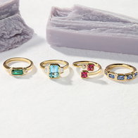Gold rings featuring rectangular and round multicolor gemstone settings displayed on a white surface.