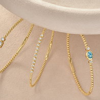 Five thin gold bracelets with gemstone accents arranged side by side on a neutral background.
