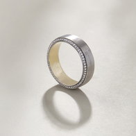 Brushed white gold wedding band with diamond pavé edges on a light background.