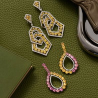 Fancy yellow diamond drop earrings and pink and yellow gemstone halo earrings styled on a green leather background.