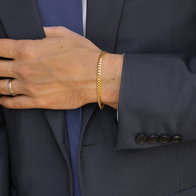 Men’s gold chain bracelet worn with a navy suit jacket.