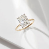 Radiant-cut diamond solitaire engagement ring with a yellow gold band displayed on a light background.